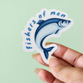 A hand holding a sticker with an illustration of a fish and the phrase 'fishers of men'.
