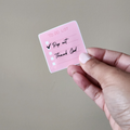 A hand holding a pink sticky note with the text 'TO DO LIST' and tahnk God a check mark, on a plain background.