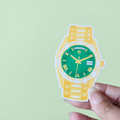 A sticker designed like a yellow and green wristwatch with the text 'On Time God' on the watch face.
