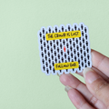 A hand holding a vinyl sticker with text and pattern design on a green background.